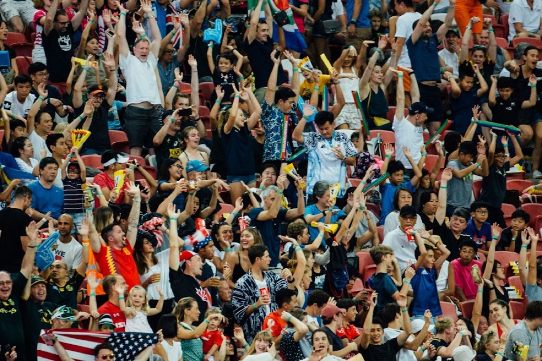 Men and women of all ages cheering with arms raised in a packed stadium